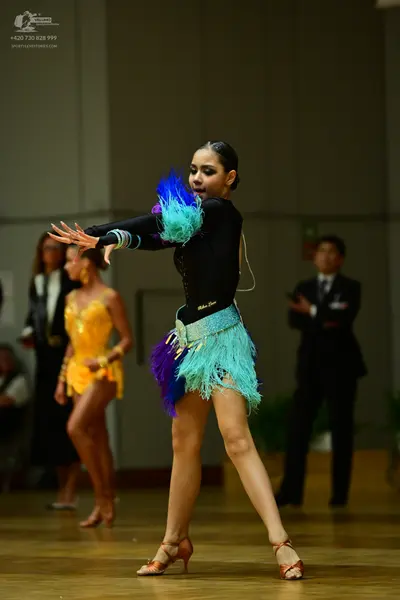 Dancesport competitor: Female dancer in foreground: black long-sleeved latin dress with colorful teal, 