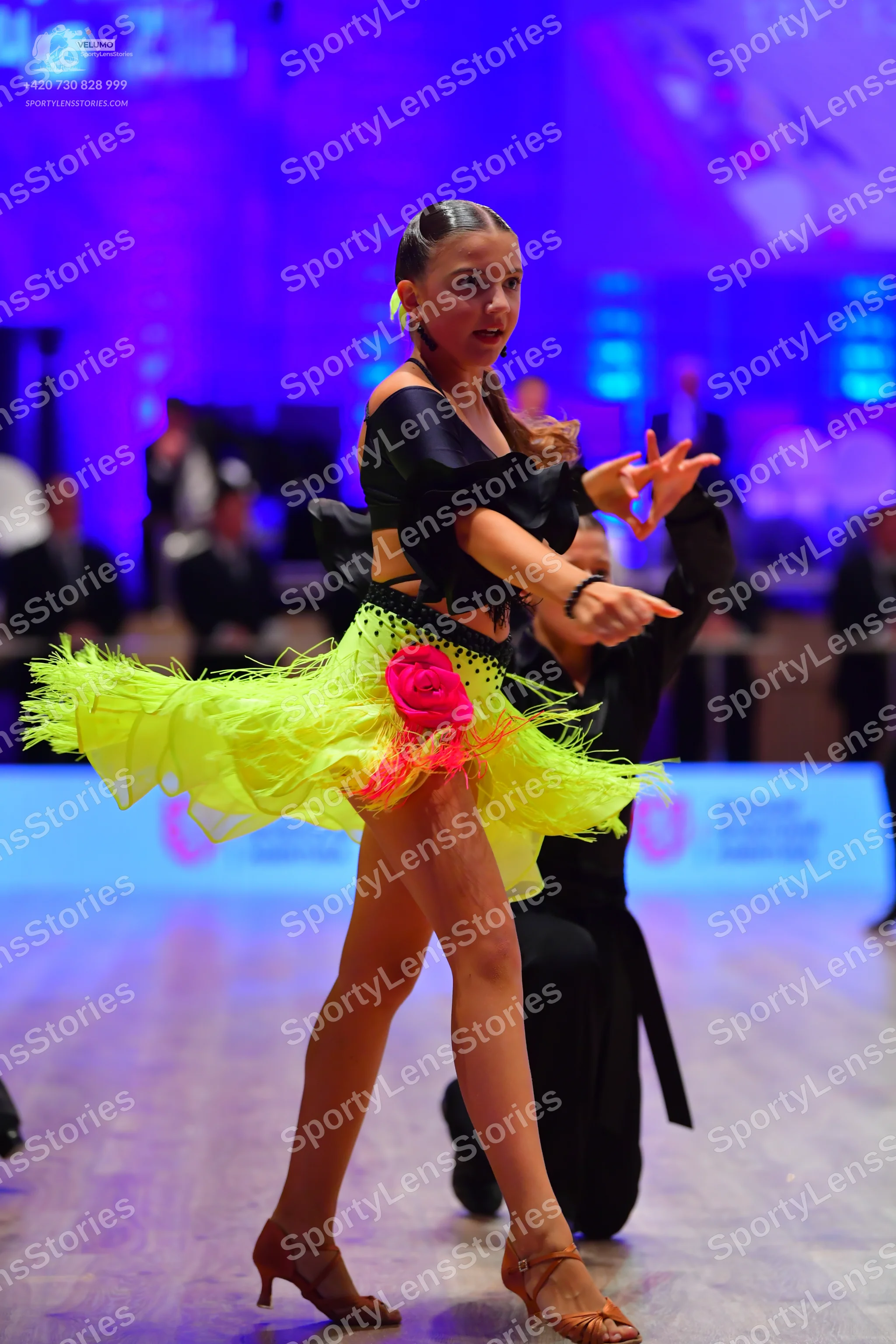 Dancesport competitor: Female dancer: black off-the-shoulder top and a neon yellow ruffled tulle skirt