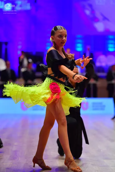 Dancesport competitor: Female dancer: black off-the-shoulder top and a neon yellow ruffled tulle skirt 