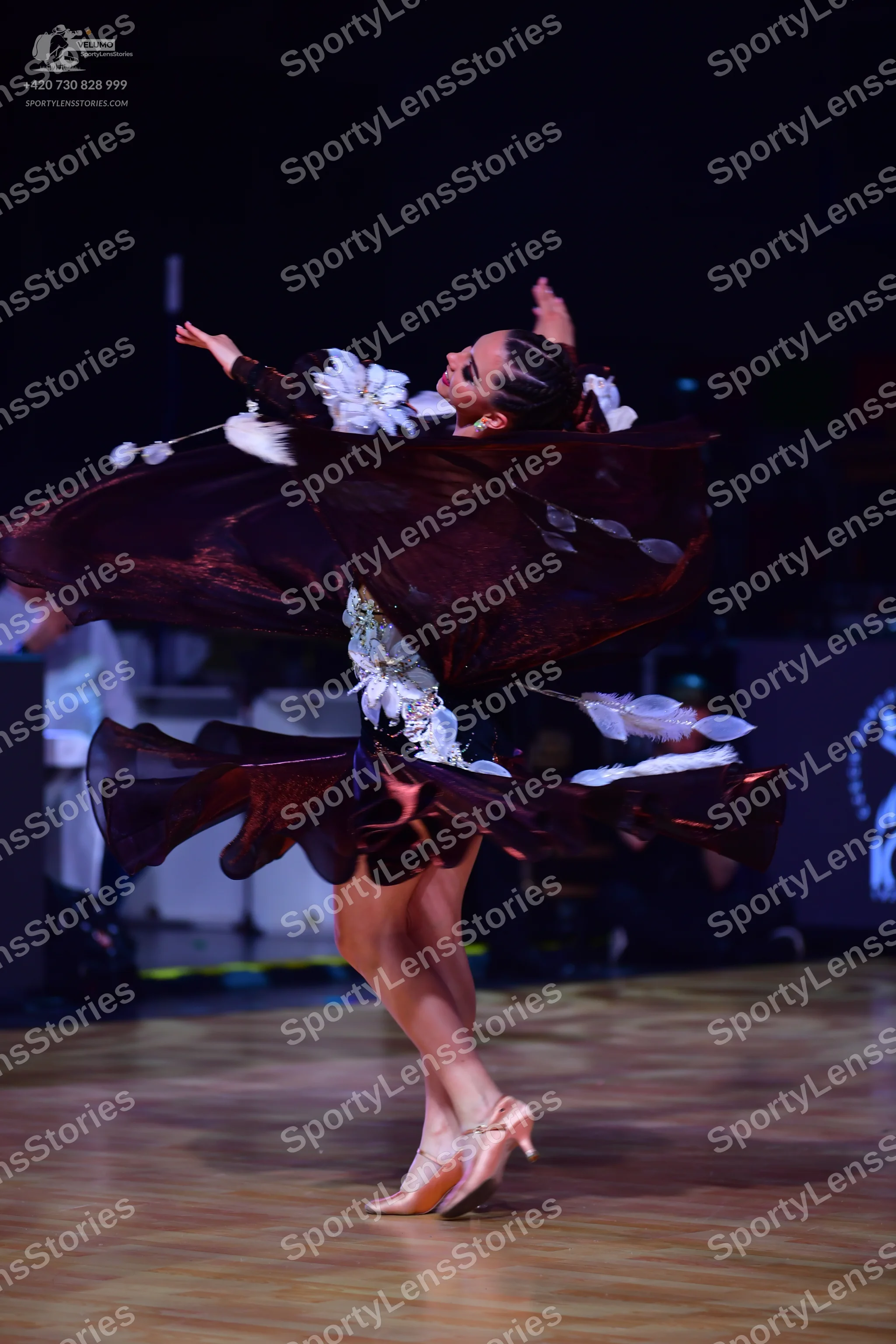 Dancesport competitor: Female dancer: dark burgundy Latin dress with large white floral or feather-like