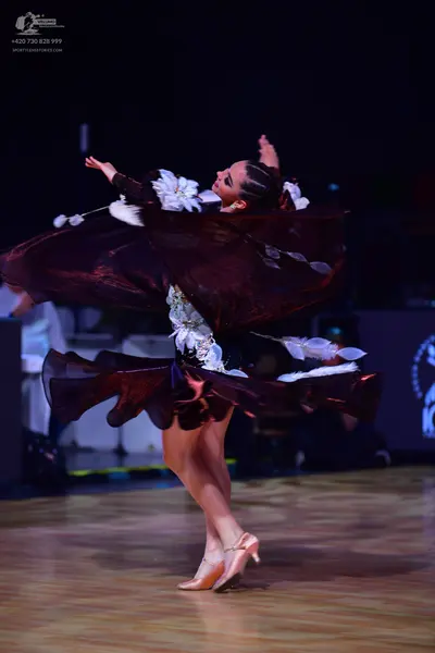 Dancesport competitor: Female dancer: dark burgundy Latin dress with large white floral or feather-like