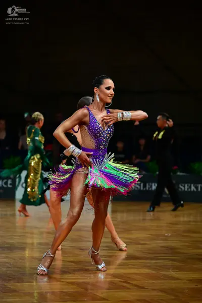 Dancesport competitor: Female dancer in foreground: purple latin dress with colorful fringe (green, pin
