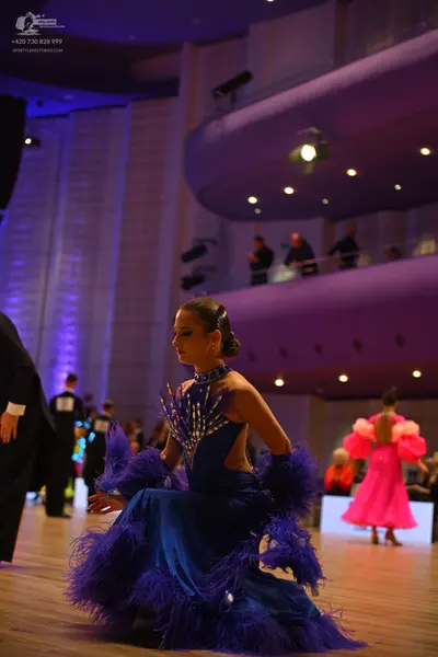 Dancesport competitor: Female dancer: blue satin latin dress with large purple feather trim