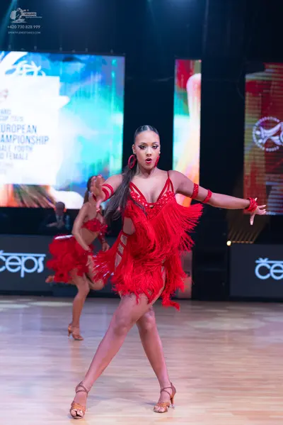 Dancesport competitor: Female dancers: matching red Latin dresses with fringe and sequins, red wristban