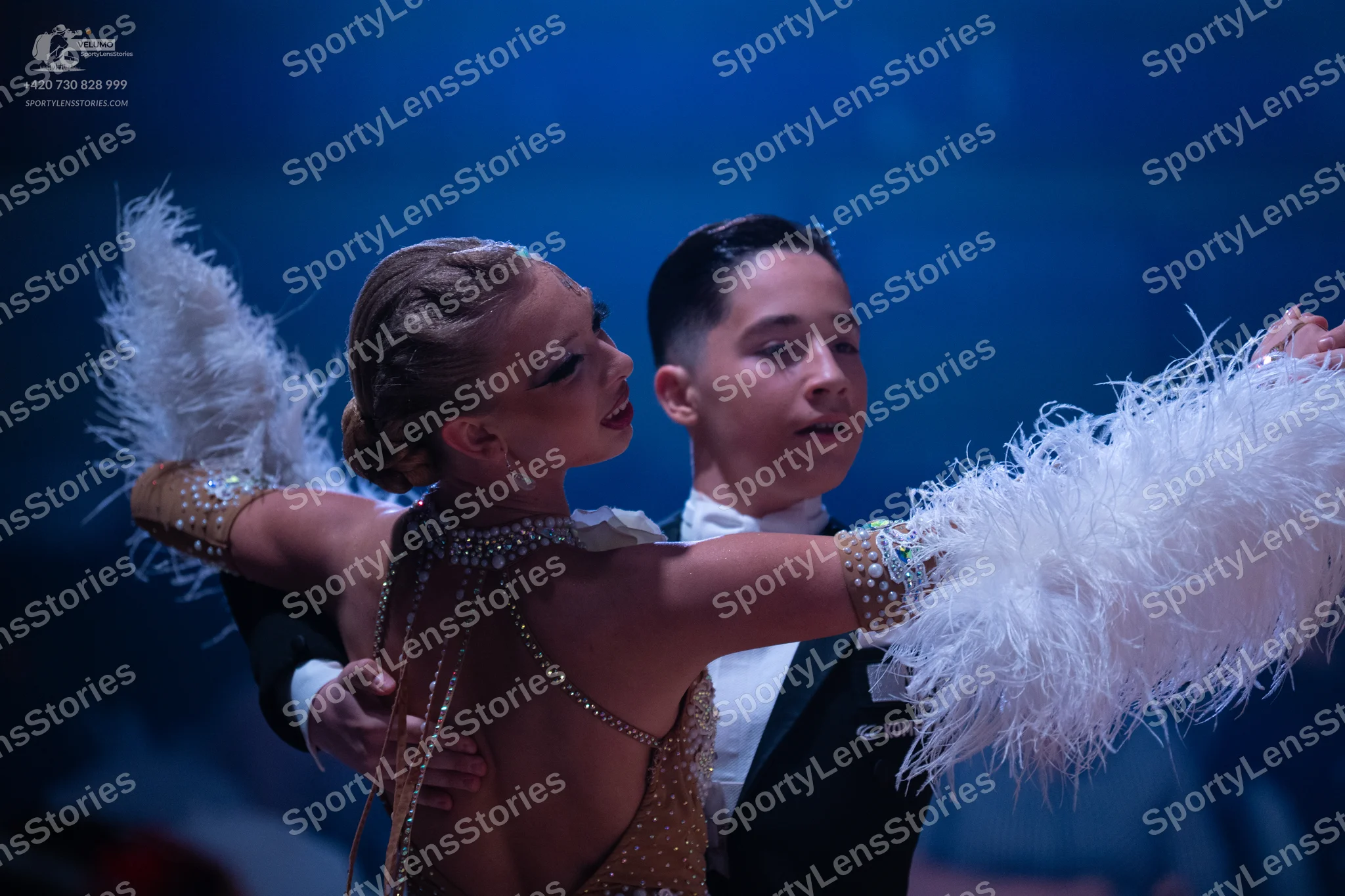 Dancesport competitor: Female dancer: gold Latin dress embellished with crystals and large white feathe