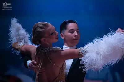 Dancesport competitor: Female dancer: gold Latin dress embellished with crystals and large white feathe